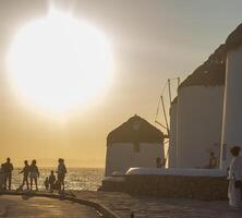 Traditional windmills with white walls and wooden structures at sunset in Mykonos, Greece. Historical architecture and travel concept. photo