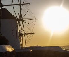 Traditional windmills with white walls and wooden structures at sunset in Mykonos, Greece. Historical architecture and travel concept. photo