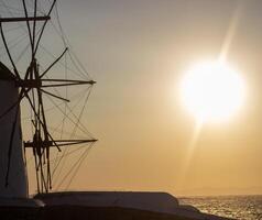 Traditional windmills with white walls and wooden structures at sunset in Mykonos, Greece. Historical architecture and travel concept. photo