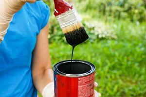 a woman's hand in a glove holds a brush with black paint flowing from it into a jar photo