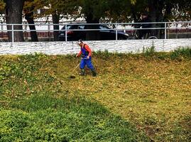 Nitra, Slovakia - 11.18.2024 A municipal worker cuts the grass using power tool string lawn trimmer on the banks of the Nitra river. photo