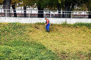 Nitra, Slovakia - 11.18.2024 A municipal worker cuts the grass using power tool string lawn trimmer on the banks of the Nitra river. photo