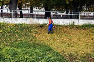 Nitra, Slovakia - 11.18.2024 A municipal worker cuts the grass using power tool string lawn trimmer on the banks of the Nitra river. photo