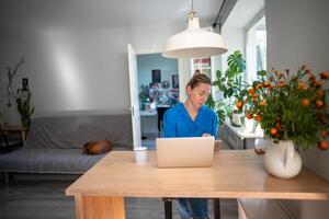 Thoughtful woman of middle age working at laptop from home office. Remote working. photo