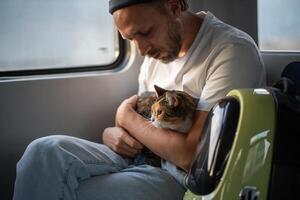 Public electric train ride of thoughtful man hugging calm peaceful fluffy cat sitting on owner lap photo