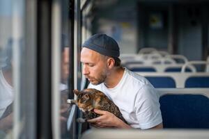 Attentive caring man pet owner traveling with fluffy cat in hands showing window in electric train. photo