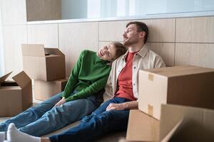 Pleasantly tired couple finished moving things in boxes for move to new house sit together on floor. photo