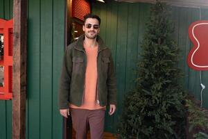 Handsome man in jacket standing outside green house during Christmas photo