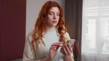 Carefree Caucasian woman girl touch screen using smartphone relaxed lady scrolling digital feed in social media Internet by mobile phone device at home calm female look in camera cyberspace connection video