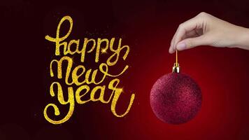 Happy New Year inscription from golden glitter and 2025 symbol on red New Year ball in a hand. On red Background motion animation 4k video