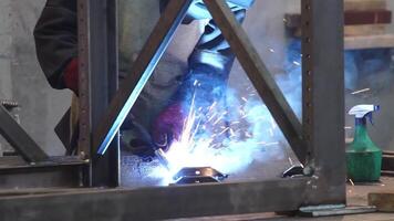Factory worker welds metal. The man is welding. Welding with argon or electrode, using a welding machine. An industrial enterprise producing metal structures. Sparks and flashes fly. video
