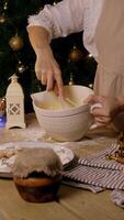 Housewife, surrounded by festive atmosphere of Christmas, is in kitchen, mixing dough with addition of egg yolks using whisk, to create dough for baking New Year's cakes and cookies. video