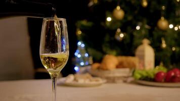 Close-up of glass filled with sparkling champagne, which is foaming and bubbling in glass, against backdrop of festive New Year's feast. Close up video