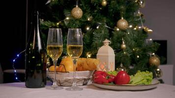 Two glasses of champagne are next to an open bottle on a New Year's eve feast, with fresh vegetables and fruits dipped in the background of the Christmas tree. video