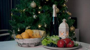 Still life of Christmas and New Year's Eve dinner table. In foreground, there are champagne, fresh vegetables, and fruits. In background, there is Christmas tree, decorated with bright garlands and toys. video