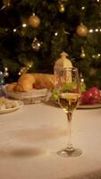Lonely glass, filled with sparkling champagne, stands on festive table, surrounded by various foods and Christmas tree, after New Year's party. video