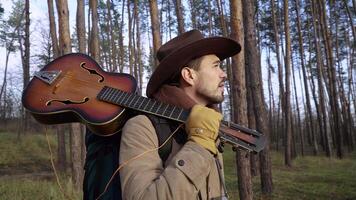 A backpacker in a hat with a guitar in the forest. Travel concept. 4K video