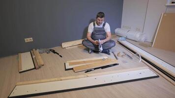 A builder in work overalls is studying the instructions for assembling a bed. Assembling furniture in a new apartment. video