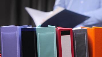 Office worker reading document with colorful ring binders in foreground video