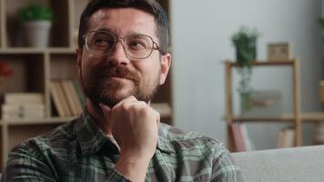 Caucasian man male guy bearded in glasses at home happy smiling pensive thinking thoughtful ponder idea smile think solution decide decision create indoors pondering hesitate unsure search answer glad video