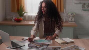 Concentrated busy pensive Hispanic woman Latina girl female lady Caucasian homeowner at home kitchen work remote distant laptop designer photograph choose apartment interior templates photos picture video