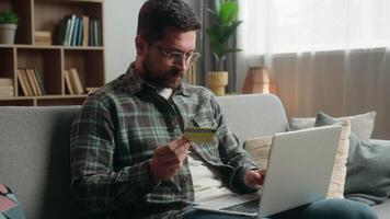 Caucasian man male guy at home happy smiling holding credit bank card buying online internet banking pay purchase shopping buying payment success achieve with laptop computer showing thumb up order video