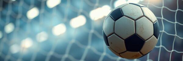 Soccer ball hits the net during an intense match in a stadium at dusk with bright lights illuminating the field photo