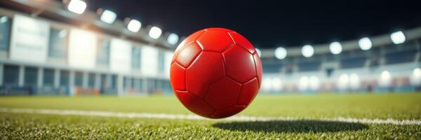 Red soccer ball rolling on a field in a stadium during a night match under bright lights photo