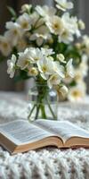 Open book placed on a table beside a vase of white flowers during the day photo