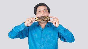 A young Indian male eating a corn cob with both hand, copy space on both sides photo