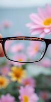 Glasses held in hand in front of colorful flowers near a serene water background on a sunny day photo