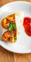 Delicious tortilla wrap filled with seasoned chicken served with a side of tangy sauce photo