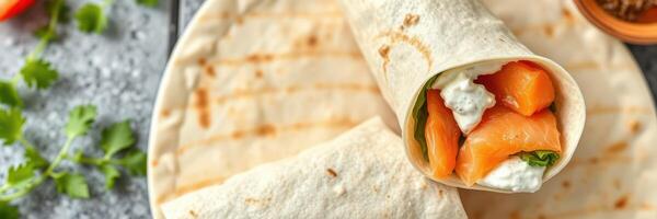 Fresh salmon wrap prepared with cream cheese and greens on a rustic surface with herbs and vegetables nearby photo