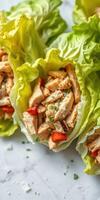 Fresh lettuce wraps filled with grilled chicken and diced vegetables served on a white marble surface photo