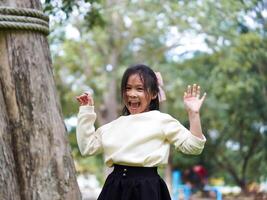 Cute little girl is peeking behind a tree, having fun playing playing peek-a-boo in a sunny garden. Smiling child in the park photo