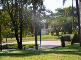A sprinkler on the lawn in autumn in a park. Watering the grass on lawn a hot sunny summer day. photo