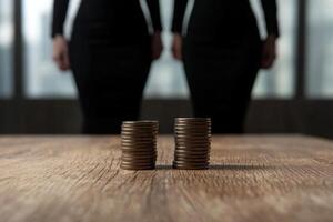 Stacks of coins on a wooden table with blurred business people in the background photo