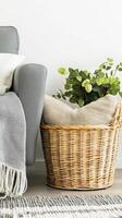 Extra rugs and cushions in basket, stylish corner accent beside grey sofa. Wicker basket near grey sofa in living room photo