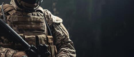 A soldier in full combat gear is standing in a dark room. He is holding a gun and looking to the side. photo