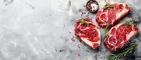 Three raw beef steaks with rosemary and spices on a gray stone background. photo