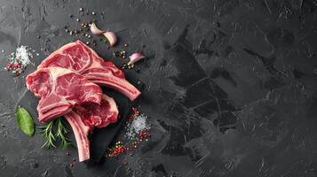 Three raw tomahawk steaks with spices on black stone cutting board. photo