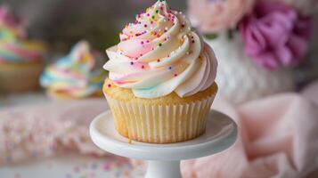 A beautifully frosted vanilla cupcake with swirls of pastel-colored buttercream and sprinkles displayed on a white stand, photo