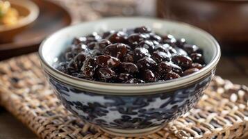 Bowl of salted fermented black beans with shiny dark surface on a woven placemat, picture photo