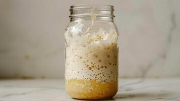 Clear jar containing bubbly sourdough starter with visible layers of flour and water mix, photo