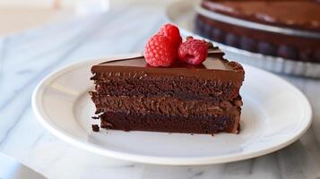 Dairy-free chocolate cake slice on a white plate topped with chocolate ganache and a fresh raspberry, photography photo