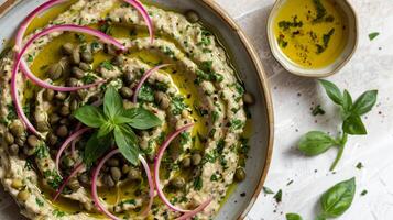 Plate of fava bean dip garnished with sliced red onions capers and a drizzle of extra virgin olive oil, photo