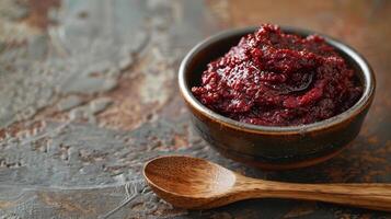 A small bowl containing deep red fermented chili paste with a wooden spoon next to it on a rustic table, photorealistic photo