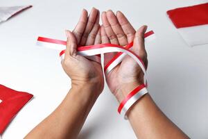 The hands of people praying are circled by a red and white ribbon photo