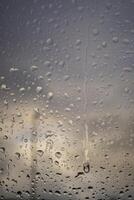 Rain drops on a window indicating gray and rainy day with defocused clouds and colors in background photo