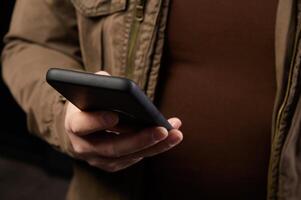 Mature man with small belly holds his smartphone in one hand while replying to message or surfing internet photo